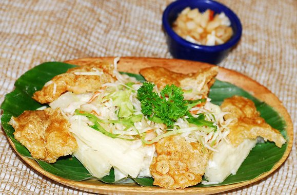 Pork rinds with yucca and coleslaw, served on a banana leaf